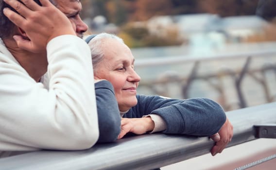 Elderly man and woman are leaning on the railing of the bridge, talking and looking at the city landscape, the old married couple happily spends together, taking care and supporting each other.