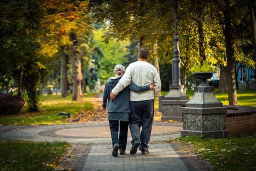 An embracing elderly couple walks in the autumn park on a sunny day, a man hugs his beloved woman and wife and actively spends time together, develop a harmonious relationship with love.