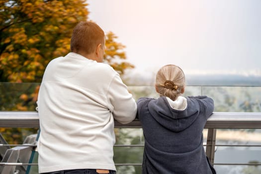 A man and a woman are walking in the park and talking, looking at a beautiful city view - a panorama. Husband and wife aged happily spend time together and support each other.