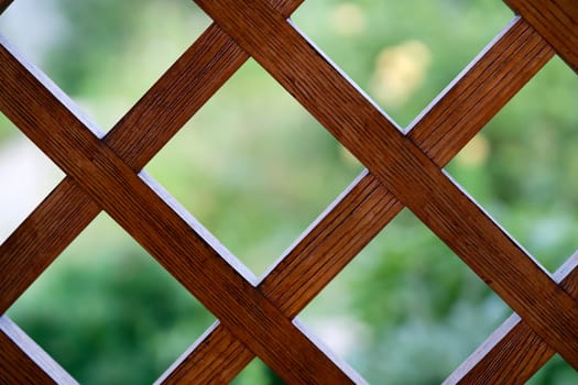 A beautiful background with a wooden lattice, a square grid, a decorative fence on a balcony or terrace against the backdrop of a summer garden, an outdoor fence with a square, rhombic pattern.