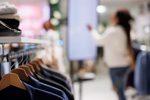 Stylish clothes hanging on rack in shopping mall with blurred background. Trendy jackets on hangers showcasing merchandise brand new collection in fashion boutique close up