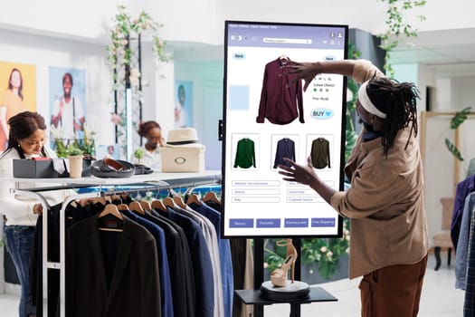 Male customer using clothing store kiosk service, choosing fashion collection items online on self ordering checkout board. Young adult slectiong clothes on interactive monitor display.