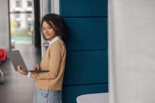 Pretty female freelancer working on laptop while standing on modern coworking background