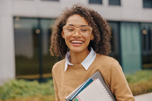 Smiling female freelancer standing with laptop and note pads on modern building backgrounds