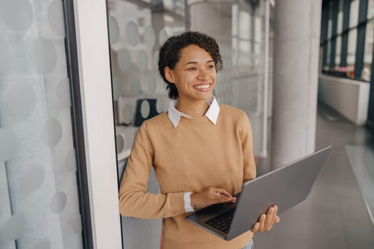 Smiling female manager using laptop while standing on office background and looks away