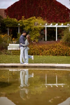 A couple in love hugs on the shore of a city pond in the European town. love story against the backdrop of autumn nature. romantic ambiance, couple goals, outdoor romance, seasonal charm, love in the city, autumnal vibes, European town, city pond, affectionate bonding, love story