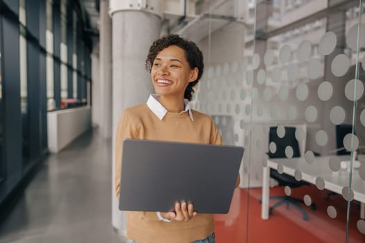 Pretty female freelancer working on laptop while standing on modern coworking background