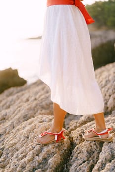 Woman in a white dress and sandals stands on the rocks. Cropped. Faceless. High quality photo