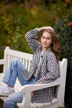 Beautiful teen blonde girl sits on a bench in an autumn park . attractive young smiling girl sitting on a bench in an autumn park. Fall Fashion Serenity: Casual Elegance in the Park