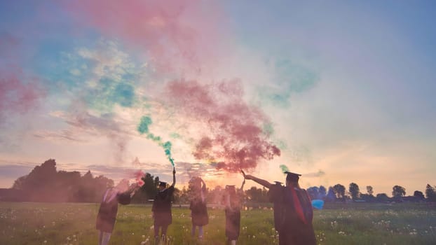 Students graduate with colored smoke walking through the meadow in the evening