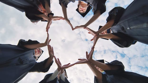 Students graduating from the college make a heart out of their hands