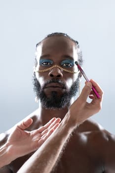 Black gay wearing make-up and hands makeup artist holding make up brush. Close up portrait homosexual man looking at camera ready for apply visage on face. Fashion lgbt concept.