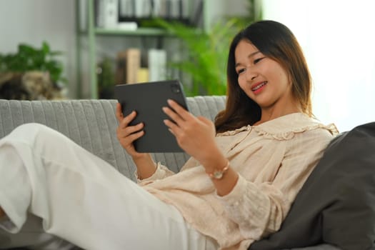 Carefree young Asian woman watching video on digital tablet. People, technology and lifestyle