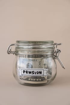 Saving Money In Glass Jar filled with Dollars banknotes. PENSION transcription in front of jar. Managing personal finances extra income for future insecurity. Beige background