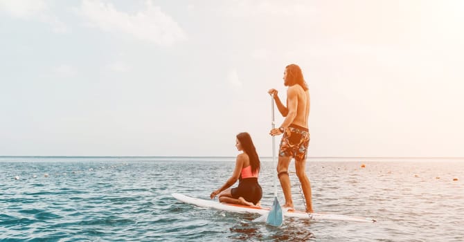 Sea woman and man on sup. Silhouette of happy young woman and man, surfing on SUP board, confident paddling through water surface. Idyllic sunset. Active lifestyle at sea or river