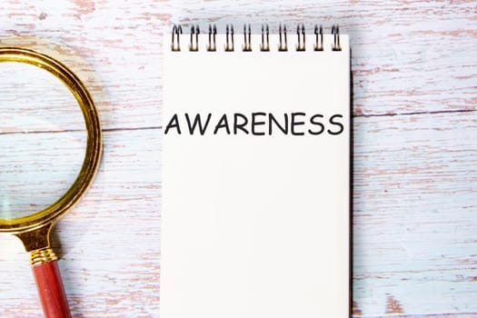 AWARENESS a word written on a notebook on wooden boards next to a magnifying glass