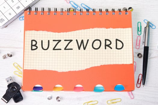 Buzzword word is written on a sheet in a cage lying on a notebook on the table next to stationery