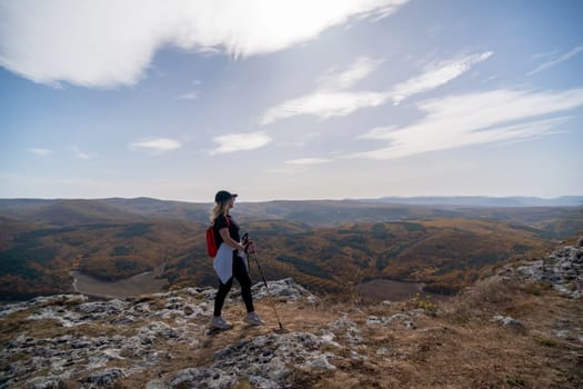 woman on mountain peak looking in beautiful mountain valley in autumn. Landscape with sporty young woman, blu sky in fall. Hiking. Nature.