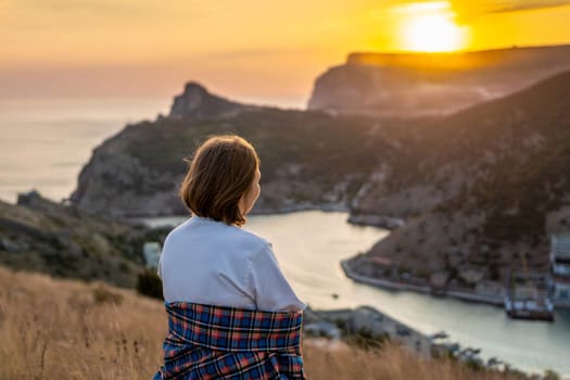 Happy woman on sunset in mountains. Woman siting with her back on the sunset in nature in summer. Silhouette