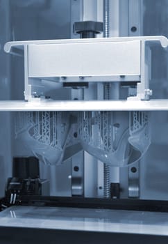 Printed models on 3D printer close-up. Objects printed on photopolymer sla 3D printer from liquid photopolymer resins on printing platform inside 3d printer. Modern progressive additive technology.