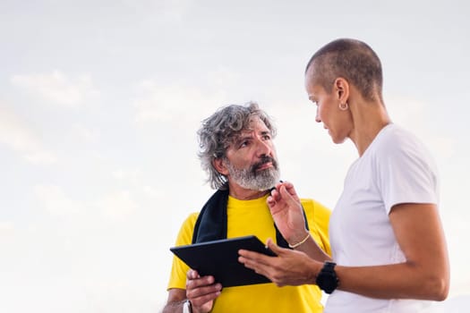 female personal trainer explaining training with tablet to an elderly sports man, concept of active and healthy lifestyle in middle age, copy space for text