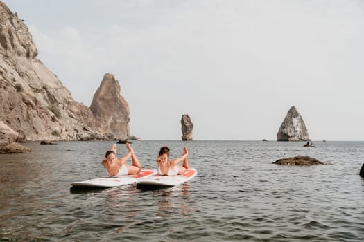 Woman sup yoga. Middle age sporty woman practising yoga pilates on paddle sup surfboard. Female stretching doing workout on sea water. Modern individual hipster outdoor summer sport activity