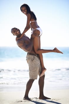 Lifting, portrait and couple at a beach with love, romance or bonding in nature together. Support, travel and black people embrace at sea with freedom, energy and excited for summer, vacation or trip.