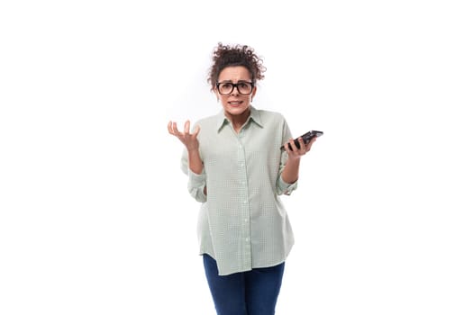 young pretty brunette woman in glasses is upset and holds a mobile phone in her hand.