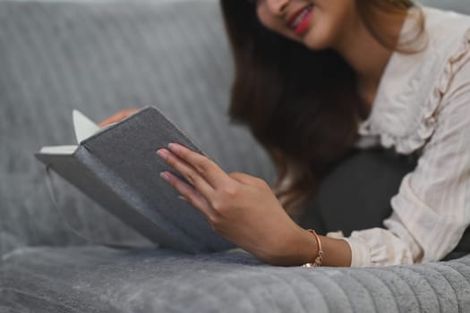 Carefree asian woman lying on couch and reading book. People, leisure and lifestyle concept.