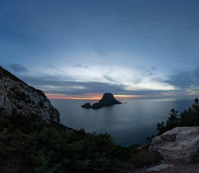 Solo traveler admires Es Vedra rock at sunset in Ibiza.