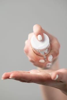 A girl in the bathroom takes care of her skin and applies cream to her body, cosmetologist squeezes cream from a jar on the hand, hand and face skin care.