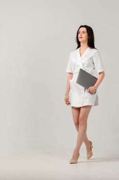a beautician girl in a white coat holds a laptop in her hands in a photo studio on a white background, portrait of a girl in a white coat.