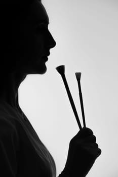 Silhouette of a girl in profile holding paintbrushes, silhouette on a white background.