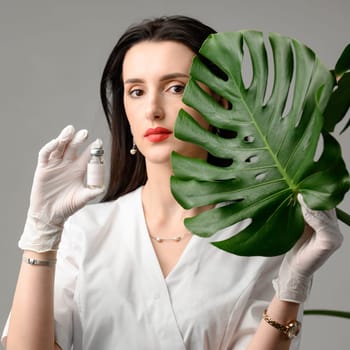 A girl holds a jar with a peeling preparation in her hands on the foreground of a monstera leaf.