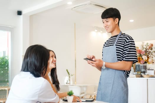 Cheerful smiling waiter in apron using table while take order and talk to clients cafe coffee shop visitors, friendly professional man server wear apron write menu choice, serving staff good customer service.