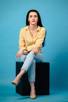 Portrait of a girl on a blue background sitting on a black cube, copy space.