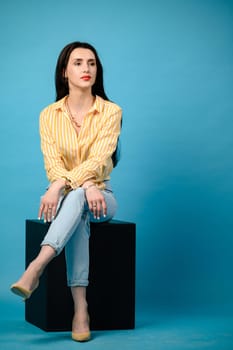 Portrait of a girl on a blue background sitting on a black cube, copy space.