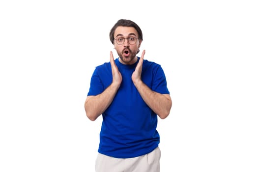 young surprised confident caucasian brunette man with a beard and glasses in a blue t-shirt on a white background.