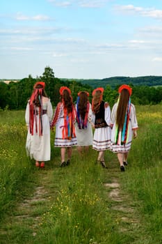 A group of girls are walking in a field, they are dressed in Ukrainian ethnic and national clothes, they have crowns with ribbons on their heads.