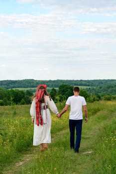 A boy and a girl walk hand in hand through the field, they are dressed in Ukrainian national clothes, a boy and a girl walk.