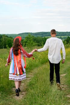 A boy and a girl walk hand in hand through the field, they are dressed in Ukrainian national clothes, a boy and a girl walk.