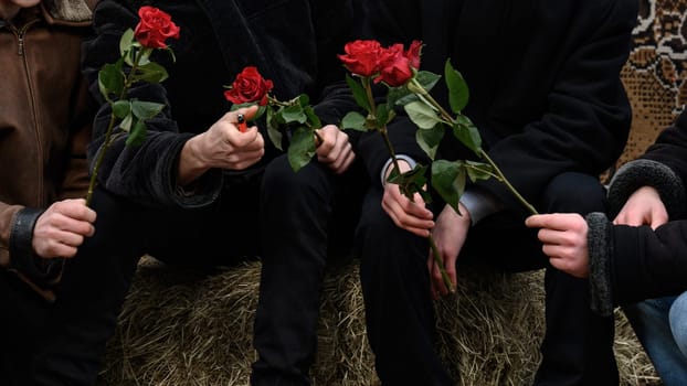 Men hold one rose, winter clothes and roses in their hands.