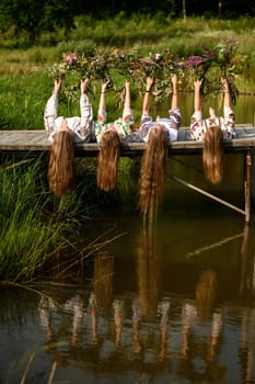 The girls are lying on the bridge near the pond and have raised woven wreaths above them, the feast of Ivan Kupala.