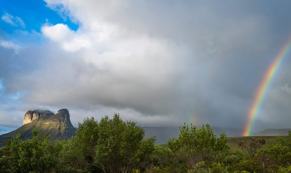 Rainbow with incoming storm clouds over a rocky outcrop in the Chapada Diamantina valleys, with space for text.