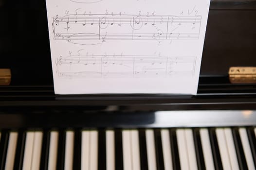 Close-up of white paper sheet with musical notes on old piano. Still life