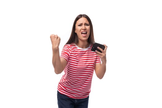 young joyful european brunette woman dressed in a striped t-shirt holding a smartphone on a white background.