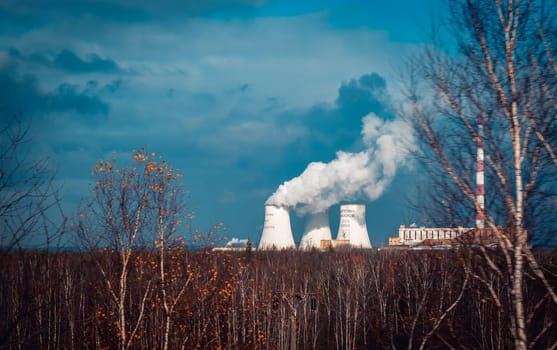 Nuclear power plant cooling towers concept photo. Big chimneys. Forest with partly cloudy sky in Polish province. Beautiful nature scenery photography. High quality picture for wallpaper, travel blog.