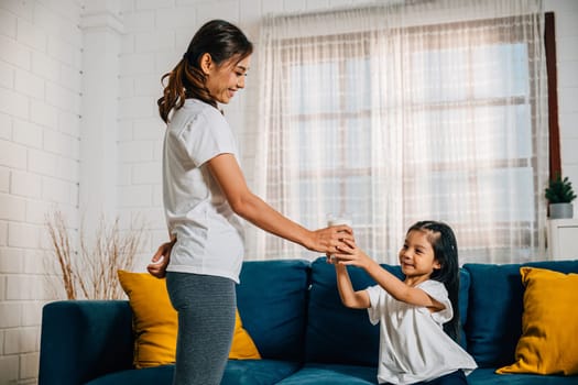 In a cozy living room an Asian mother shares a glass of milk with her daughter on the sofa celebrating the joy of togetherness promoting the importance of calcium and nurturing their strong bond.