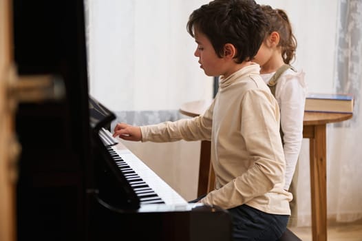 Handsome elementary age kids a teenage boy and little child girl, playing grand piano together during a music lesson at home. People. Education. Lifestyles. Hobbies. Arts, cultures and education