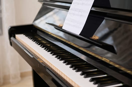 Close-up shot of old black piano with open keyboard and paper sheet with notes